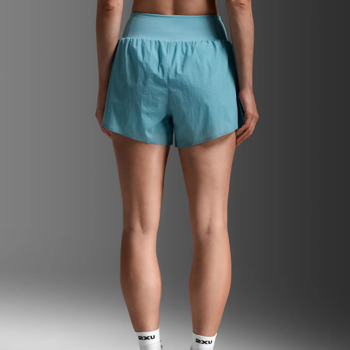 Person wearing teal athletic shorts and white socks with a brand logo on a gray background